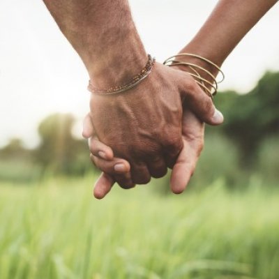 A couple holding hands while walking on the grass.